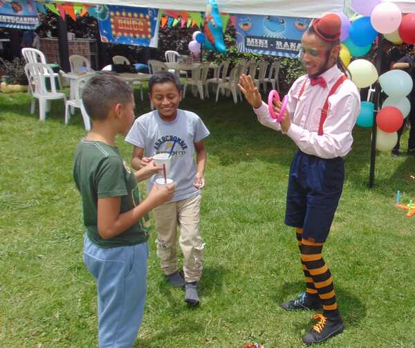 Payaso realizando magia para niños en fiesta infantil en jardín.