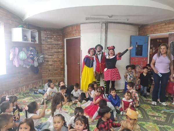 Niños en taller de refuerzo preescolar con payasos en aula escolar.