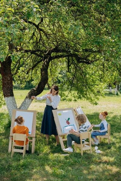 Niña pintando al aire libre bajo un árbol en un taller para niños pequeños.