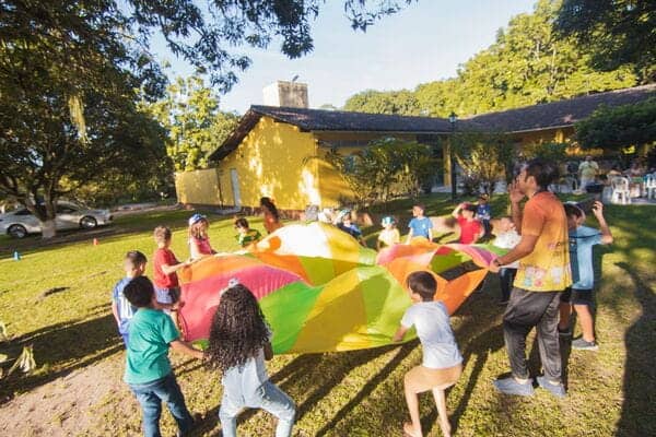 Niños jugando con paracaídas en un parque al aire libre.