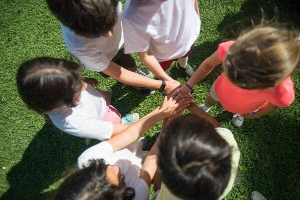 Niños jugando en césped, formando un círculo con las manos juntas.